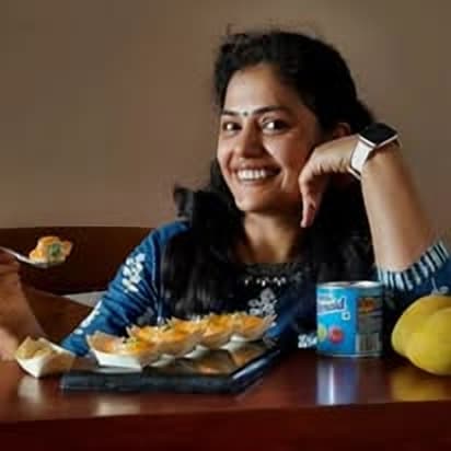 Kajal, founder and baker of Yummy Classic Delights, smiling at her kitchen table